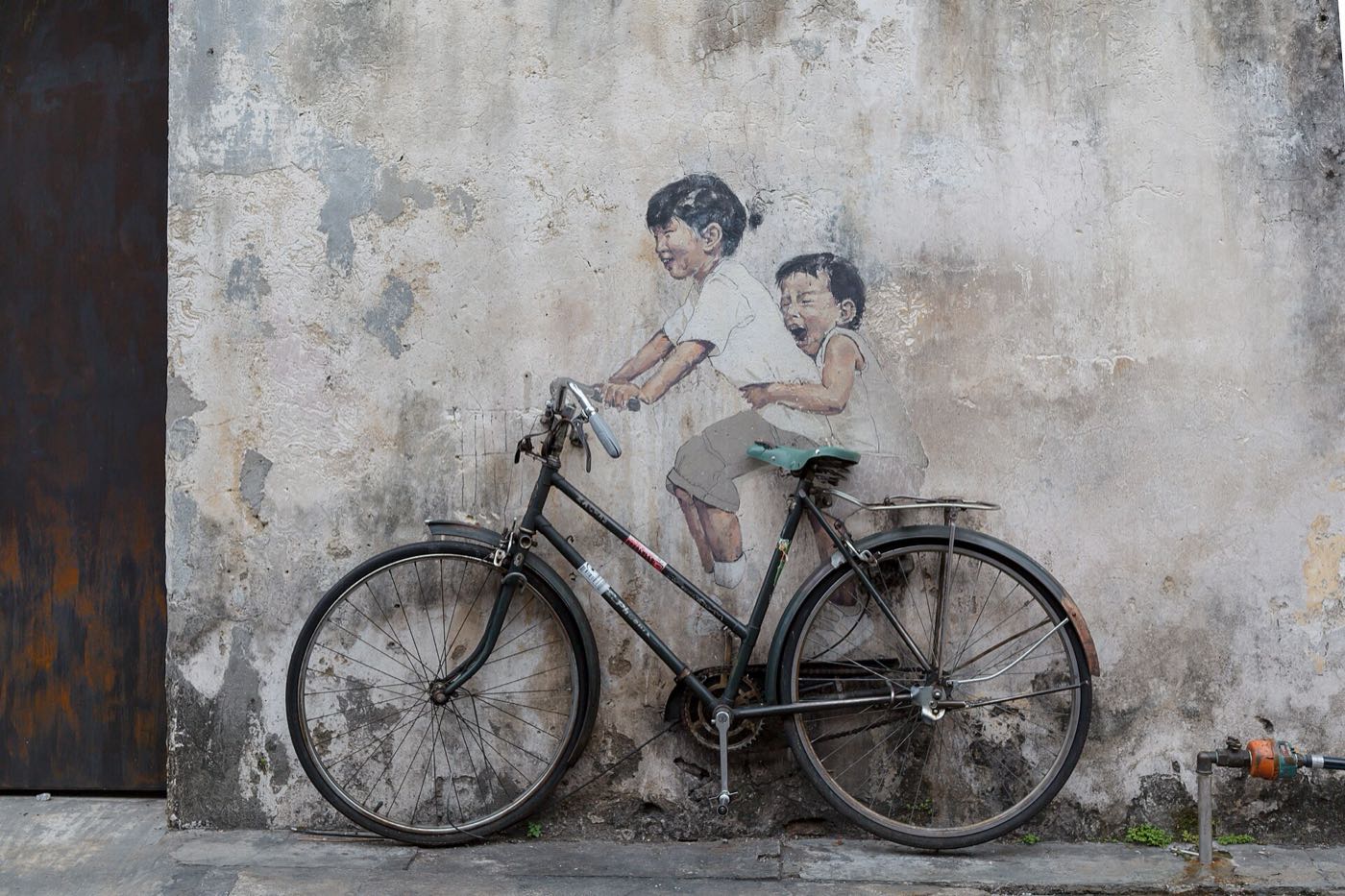 George Town mural of two children riding a real bicycle fixed to the wall